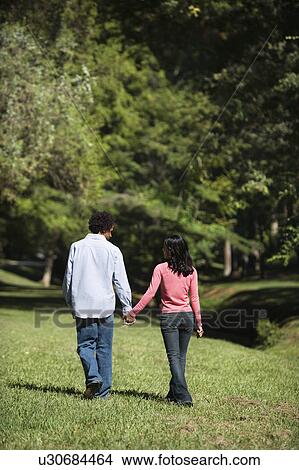 Couple holding hands walking and talking in park. View Large Photo Image Picture - Couple holding hands walking and talking in park.. Fotosearch