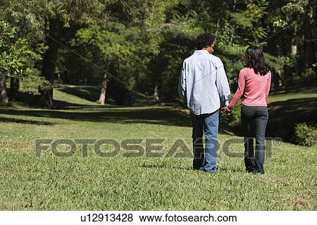 Couple holding hands walking and talking in park View Large Photo Image Stock Photo - Couple holding hands walking and talking in park. Fotosearch