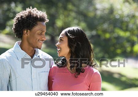 Stock Image - Couple in park looking at each other smiling. Fotosearch