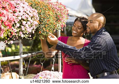 Stock Image - Happy smiling couple picking out flowers at outdoor plant market. Fotosearch
