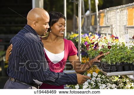 Stock Photo - Happy smiling couple picking out flowers at outdoor plant market.. Fotosearch