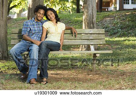 Stock Photo - Happy smiling couple sitting on park bench together. Fotosearch