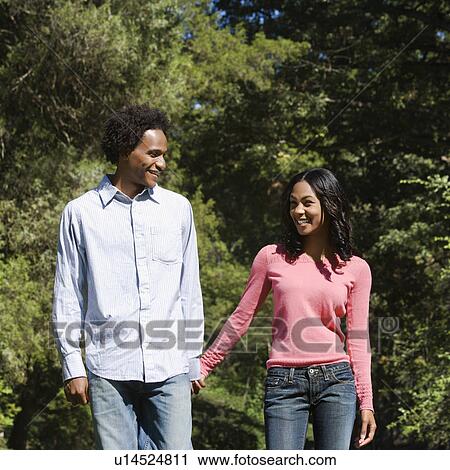 Smiling couple holding hands walking and talking in park. View Large Photo Image Stock Image - Smiling couple holding hands walking and talking in park.. Fotosearch