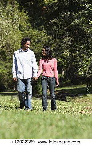 Stock Photo - Smiling couple holding hands walking and talking in park.. Fotosearch