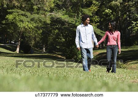 Stock Photo - Smiling couple holding hands walking and talking in park. Fotosearch