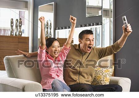 Couple cheering while watching television View Large Photo Image Stock Photography - Couple cheering while watching television. Fotosearch