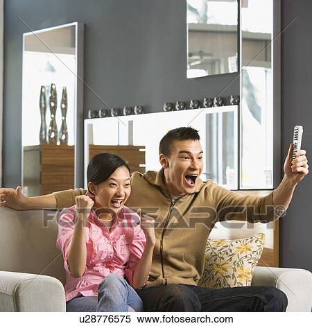Stock Photography - Couple sitting on a couch cheering. Fotosearch