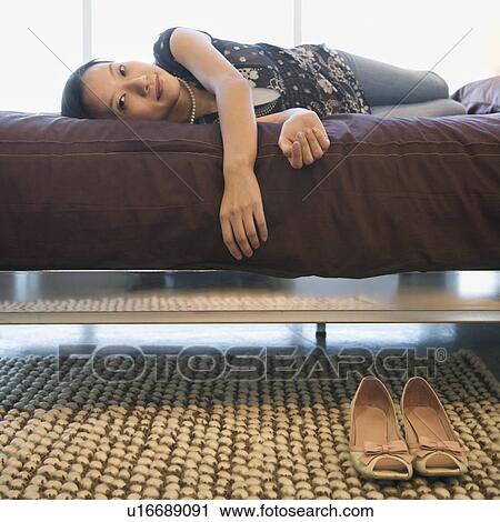 Stock Image - Portrait of Asian female lying on bed looking at viewer.. Fotosearch