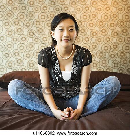 Stock Image - Portrait of Asian female sitting on bed looking at viewer.. Fotosearch