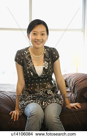 Picture - Portrait of female sitting on bed.. Fotosearch
