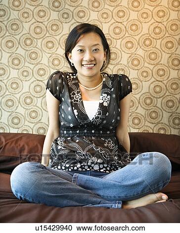 Stock Image - Portrait of woman sitting on bed looking at viewer.. Fotosearch