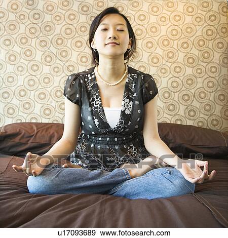 Stock Photo - Woman meditating on a bed. Fotosearch