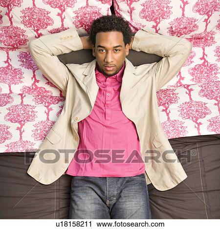 Stock Image - Young man laying on bed looking at viewer.. Fotosearch