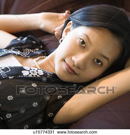 Stock Image - Young woman laying on bed looking at viewer. Fotosearch