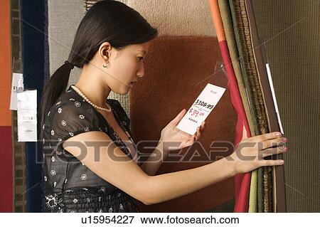 Stock Photo - Young woman shopping rugs in retail store. Fotosearch