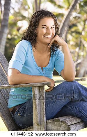 Stock Image - Female sitting in chair with hand on chin smiling. Fotosearch