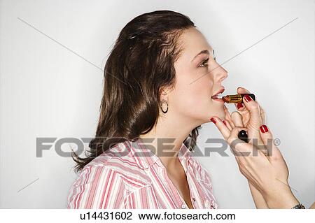 Stock Image - Hands applying lipstick to young woman. Fotosearch