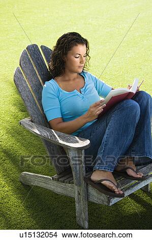 Picture - Portrait of pretty young adult brunette female sitting in chair reading book.. Fotosearch