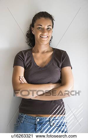 Stock Image - Portrait of pretty young adult brunette female with arms crossed smiling and looking at viewer. Fotosearch