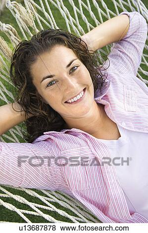 Stock Photo - Pretty young adult brunette female laying in hammock with hands behind head smiling at viewer.. Fotosearch