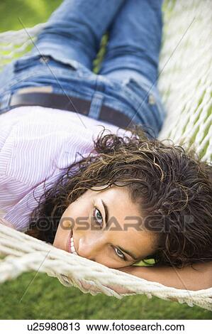 Stock Image - Smiling pretty young adult brunette female lying in hammock looking up at viewer. Fotosearch
