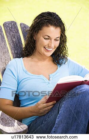 Stock Image - Smiling woman sitting and reading a book. Fotosearch