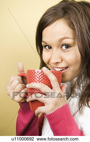 Stock Image - Woman holding coffee cup to lips and smiling at viewer. Fotosearch