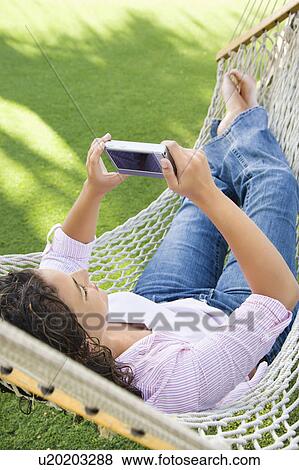 Stock Photo - Woman lying in hammock using PDA. Fotosearch