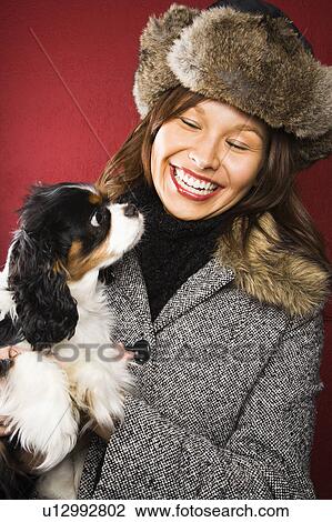 Stock Image - Woman wearing fur hat holding King Charles Spaniel. Fotosearch