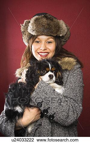 Stock Image - woman wearing fur hat holding King Charles Spaniel in arms . Fotosearch