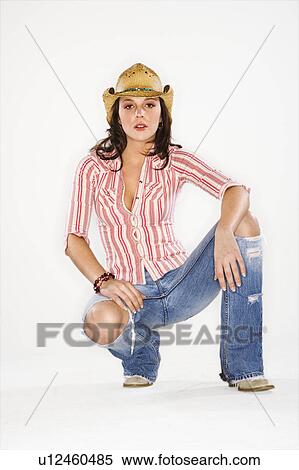 Stock Photography - Young Caucasian woman wearing cowboy hat crouching and looking at viewer.. Fotosearch