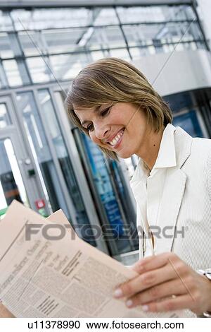 Stock Image - Woman reading newspaper smiling. Fotosearch