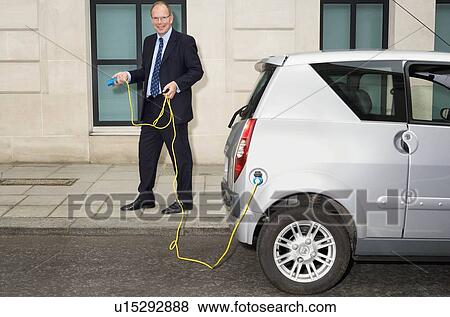 Stock Photo - Man holding cable for electric car. Fotosearch