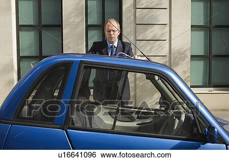 Man looking at papers on top of car View Large Photo Image Stock Photograph - Man looking at papers on top of car. Fotosearch