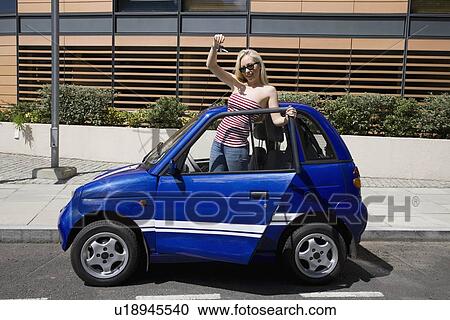 Young woman waving by electric car View Large Photo Image Stock Image - Young woman waving by electric car. Fotosearch