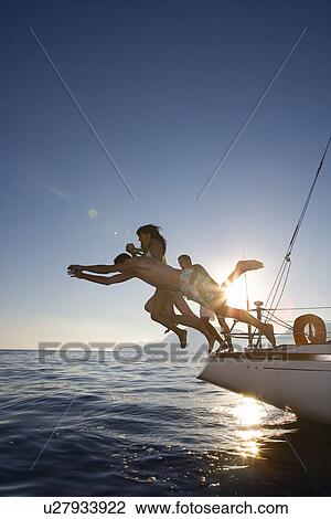 Stock Image - Group dive off back of sailboat. Fotosearch