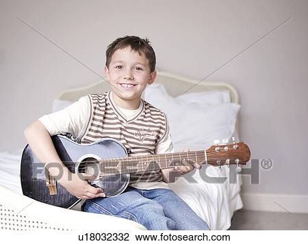 Young boy sitting on bed playing guitar View Large Photo Image Stock Image - Young boy sitting on bed playing guitar. Fotosearch