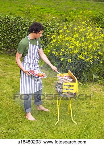 Young man placing meat on barbecue View Large Photo Image Stock Image - Young man placing meat on barbecue. Fotosearch