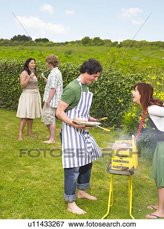 Stock Photo - Young man tending barbecue with friends. Fotosearch