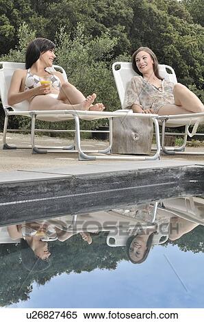 Two women relaxing by the swimming pool View Large Photo Image Stock Photography - Two women relaxing by the swimming pool. Fotosearch