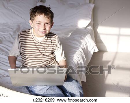Boy sitting in bedroom with laptop View Large Photo Image Stock Photo - Boy sitting in bedroom with laptop. Fotosearch