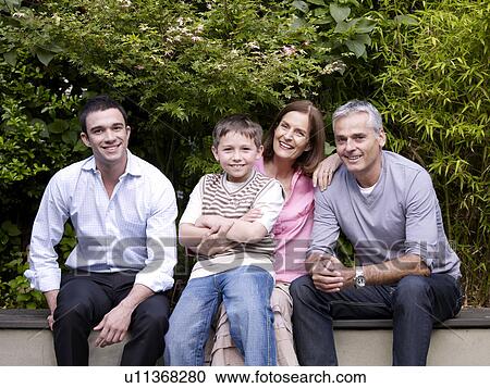 Stock Image - Family sitting together in garden. Fotosearch
