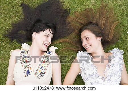 Stock Photo - 2 women laying on grass, laughing. Fotosearch