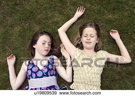 Girls lying on grass with earphones View Large Photo Image Stock Photo - Girls lying on grass with earphones. Fotosearch