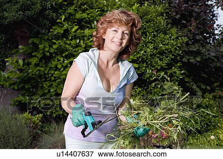 Stock Photo - Mature woman holding plants in garden. Fotosearch