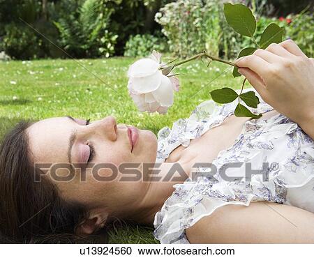 Woman laying on grass, smelling a rose View Large Photo Image Stock Image - Woman laying on grass, smelling a rose. Fotosearch
