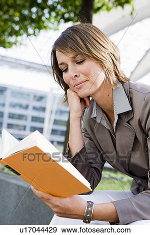 Woman sitting outdoors reading book View Large Photo Image Stock Photo - Woman sitting outdoors reading book. Fotosearch