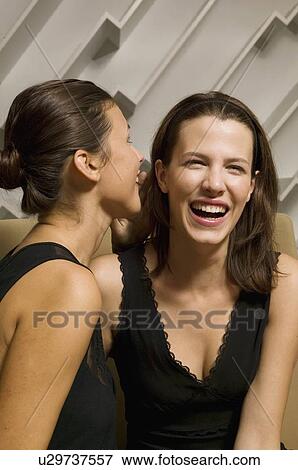 Stock Photo - Woman whispering into girlfriend's ear. Fotosearch