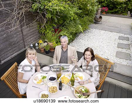 Stock Photo - Family sitting having lunch in garden. Fotosearch