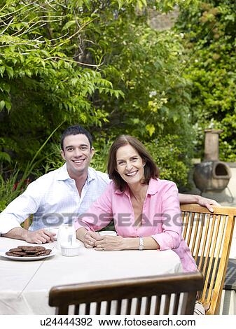 Stock Image - Man and woman sitting at table in garden. Fotosearch